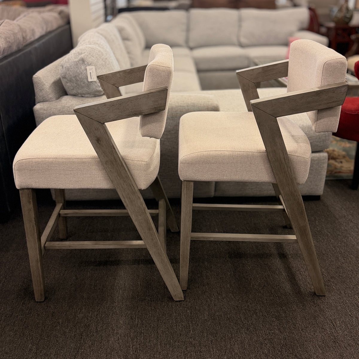 A pair of contemporary counter-height barstools featuring light oat upholstered seats and backs with angular weathered-wood frames in excellent condition.