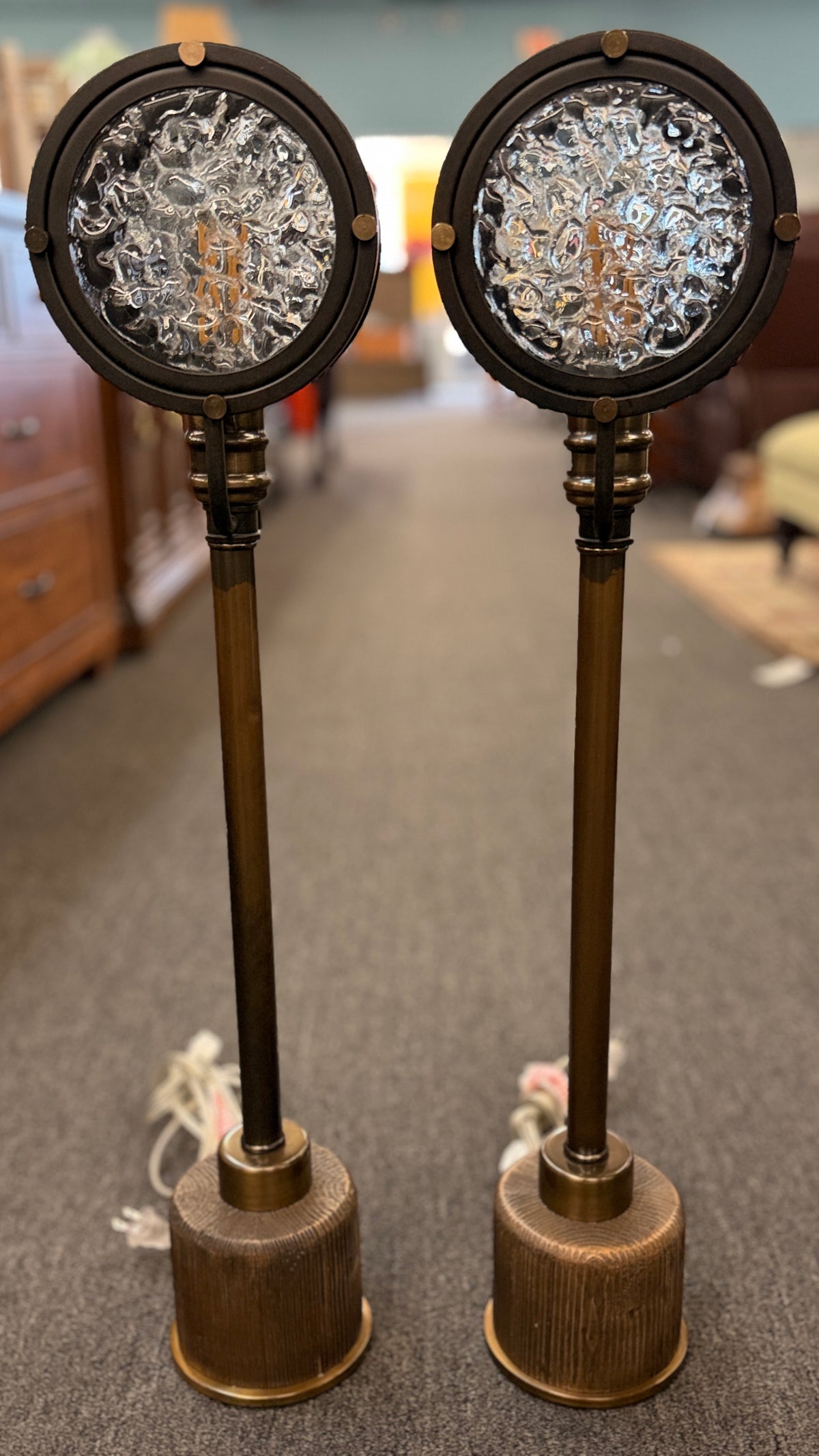 Pair of industrial-style tall table or buffet lamps featuring antiqued bronze and brass metal stems, ribbed bases, and round porthole or spotlight heads with textured glass lenses in excellent condition.