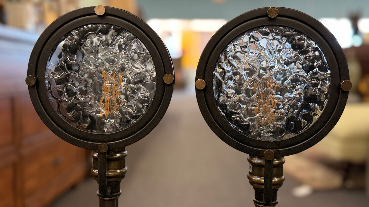 Pair of industrial-style tall table or buffet lamps featuring antiqued bronze and brass metal stems, ribbed bases, and round porthole or spotlight heads with textured glass lenses in excellent condition.