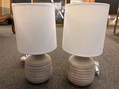 A pair of matching table lamps featuring rounded textured ceramic bases and simple white drum shades in excellent condition.