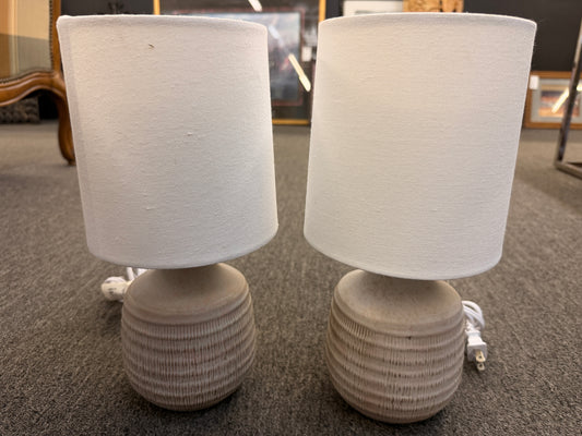 A pair of matching table lamps featuring rounded textured ceramic bases and simple white drum shades in excellent condition.