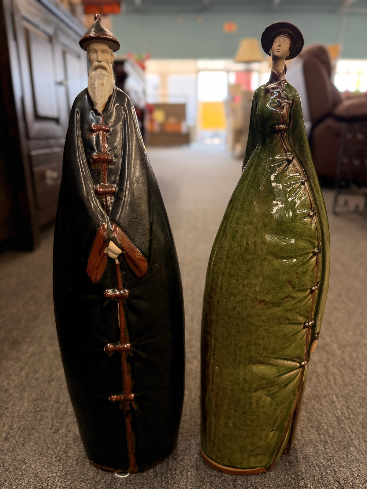 Two tall stylized ceramic figurines of standing figures, one finished in a dark glaze and the other in green in excellent condition.