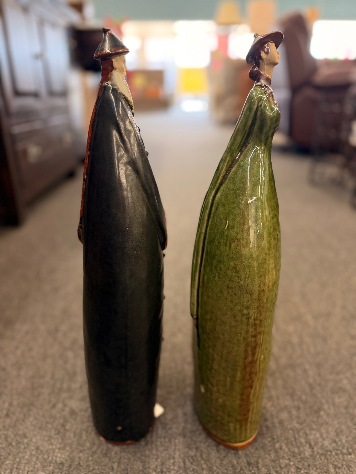 Two tall stylized ceramic figurines of standing figures, one finished in a dark glaze and the other in green in excellent condition.