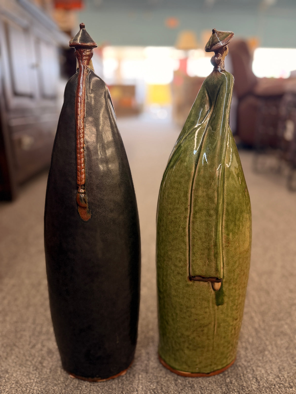 Two tall stylized ceramic figurines of standing figures, one finished in a dark glaze and the other in green in excellent condition.