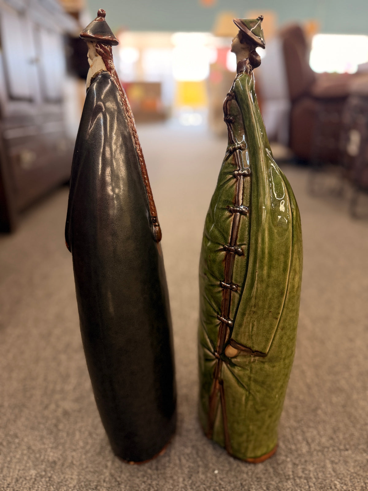 Two tall stylized ceramic figurines of standing figures, one finished in a dark glaze and the other in green in excellent condition.