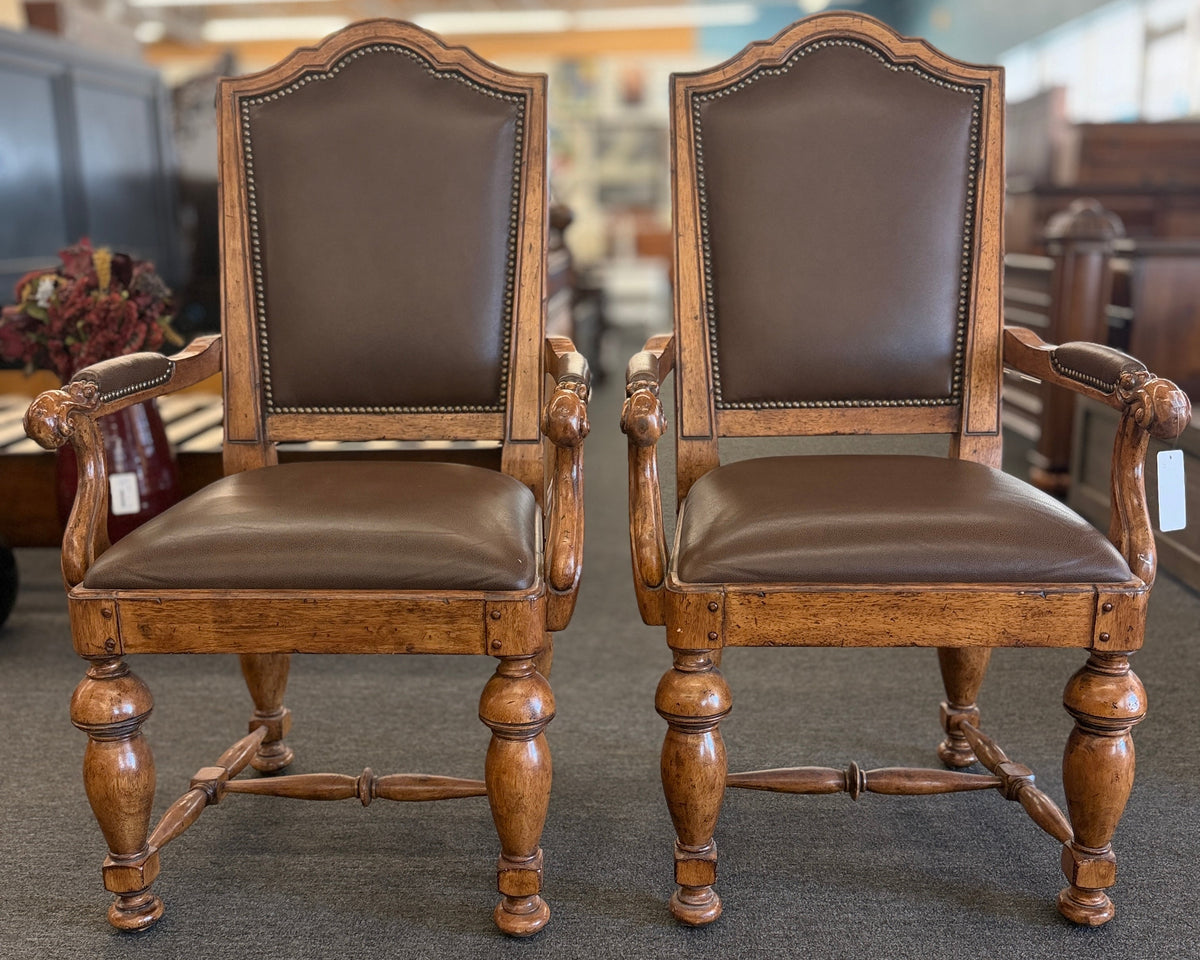 Pair of traditional wooden armchairs featuring high arched backs, brown leather upholstery accented with nailhead trim, and turned legs with stretchers in excellent condition.