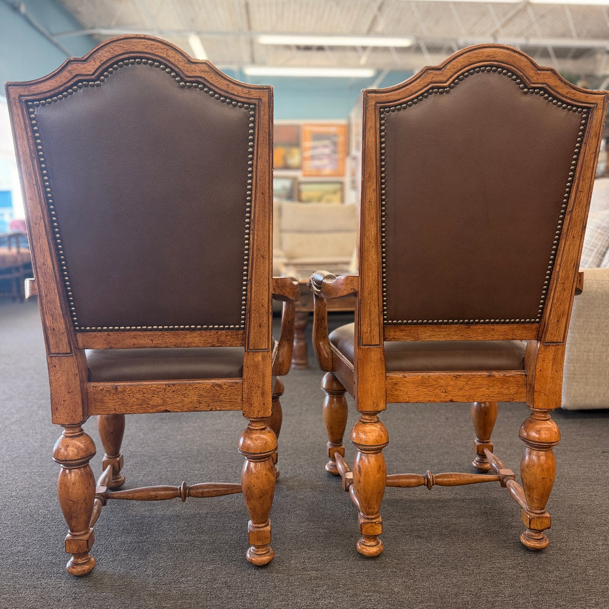Pair of traditional wooden armchairs featuring high arched backs, brown leather upholstery accented with nailhead trim, and turned legs with stretchers in excellent condition.