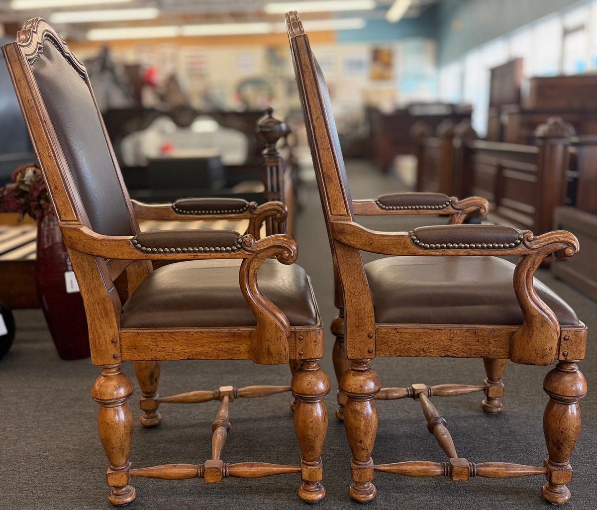 Pair of traditional wooden armchairs featuring high arched backs, brown leather upholstery accented with nailhead trim, and turned legs with stretchers in excellent condition.