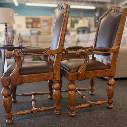 Pair of traditional wooden armchairs featuring high arched backs, brown leather upholstery accented with nailhead trim, and turned legs with stretchers in excellent condition.