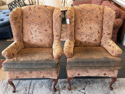 Pair of traditional wingback accent chairs upholstered in tan and brown paisley fabric with curved Queen Anne-style wooden legs.