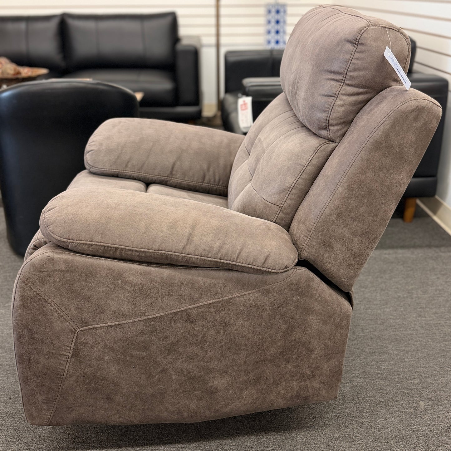 A plush, overstuffed recliner chair in a soft, medium-brown fabric with thickly padded pillow-top armrests and deep back cushioning.