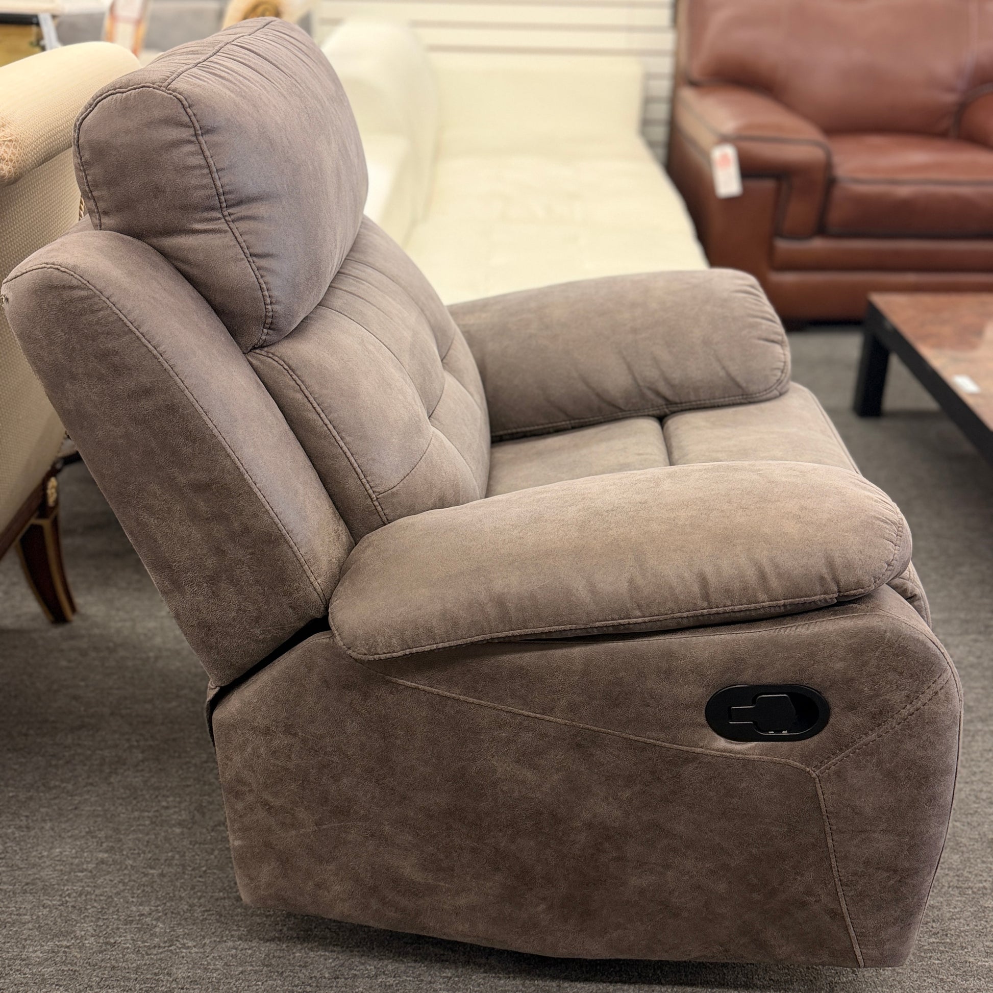 A plush, overstuffed recliner chair in a soft, medium-brown fabric with thickly padded pillow-top armrests and deep back cushioning.