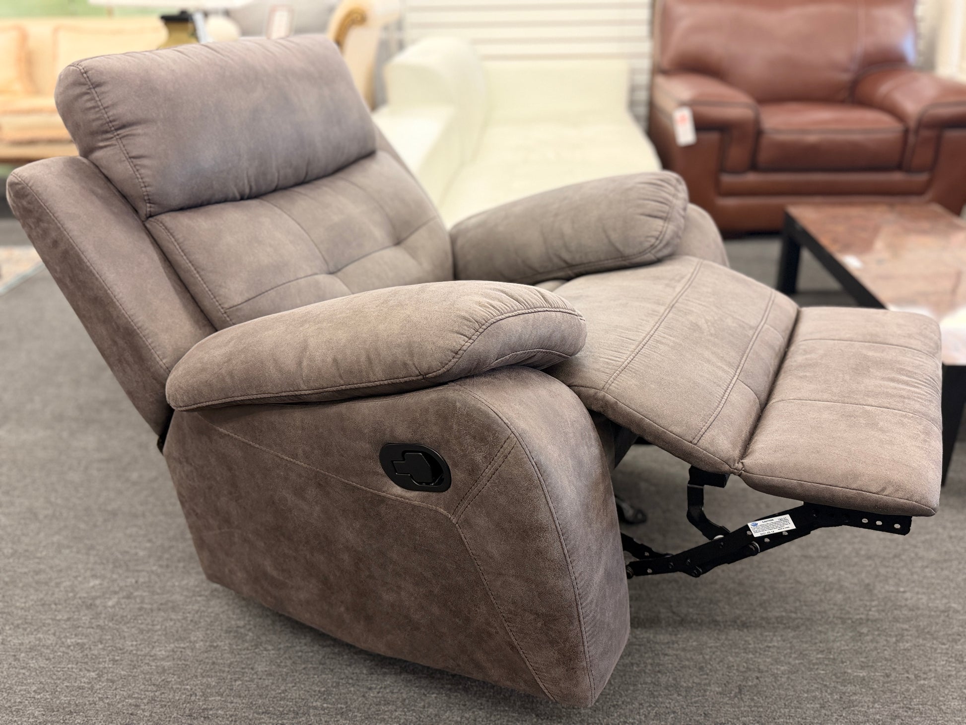 A plush, overstuffed recliner chair in a soft, medium-brown fabric with thickly padded pillow-top armrests and deep back cushioning.