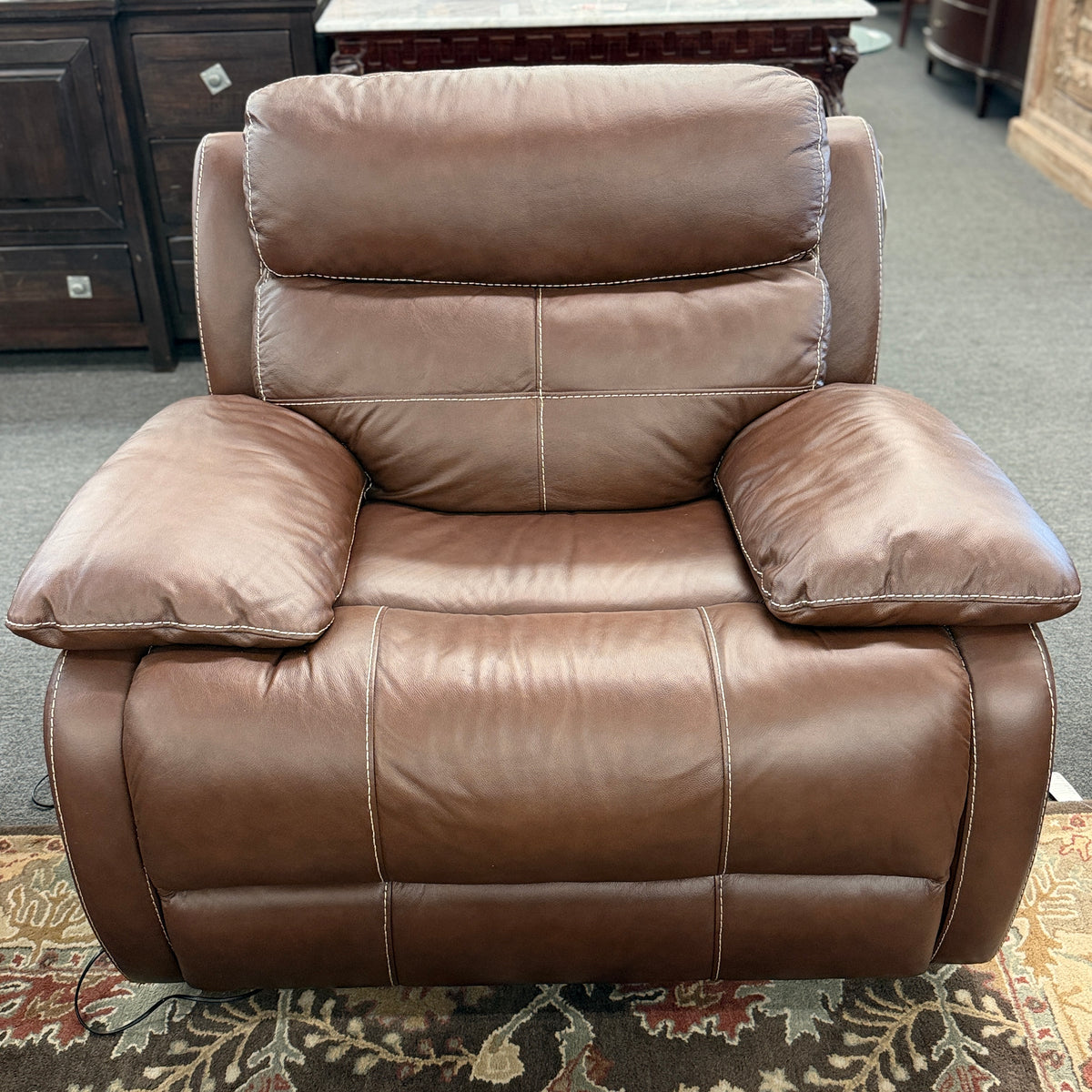 A large plush contemporary recliner upholstered in saddle brown leather with pillow-top armrests, segmented back cushioning, and light topstitching in excellent condition.