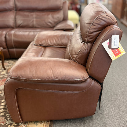 A large plush contemporary recliner upholstered in saddle brown leather with pillow-top armrests, segmented back cushioning, and light topstitching in excellent condition.