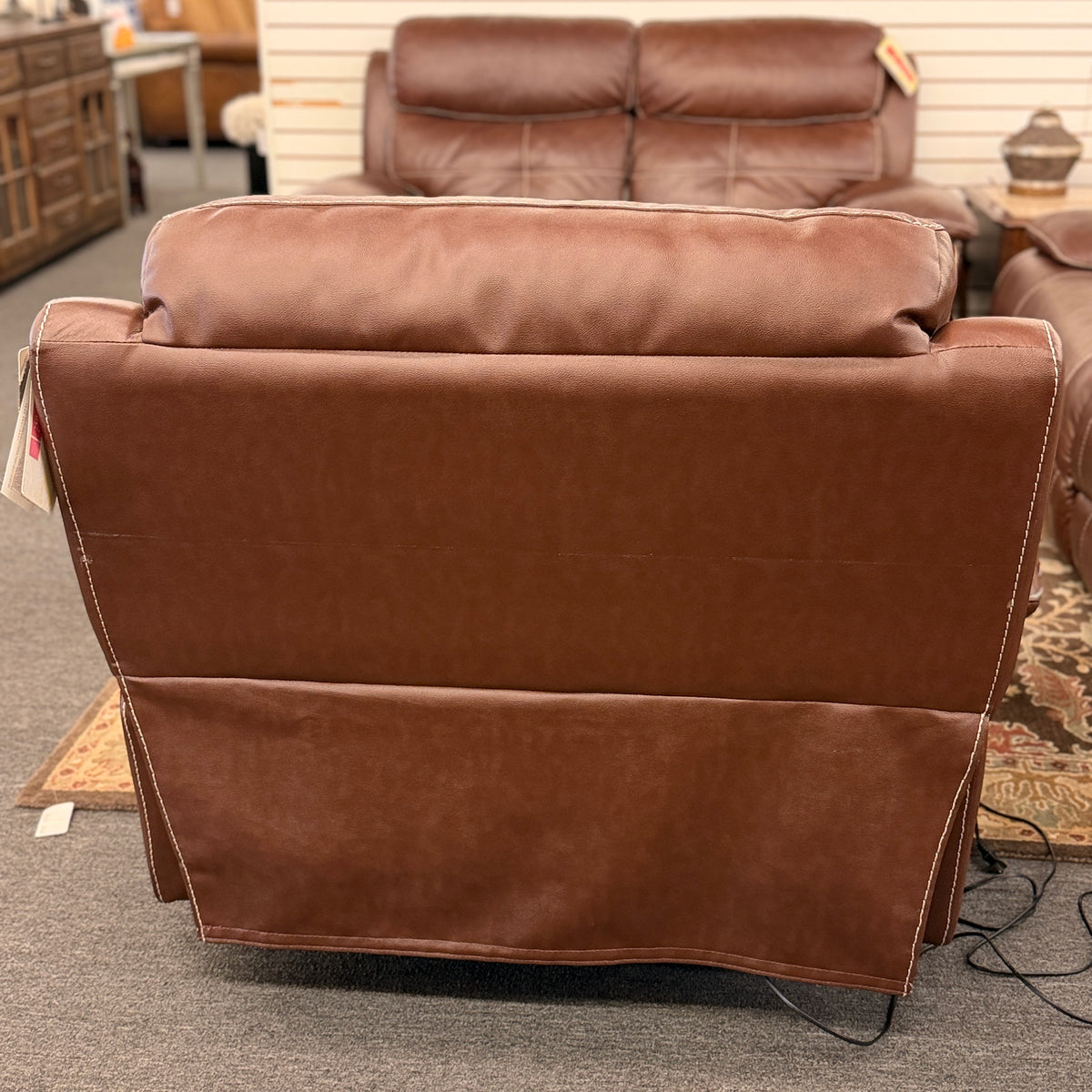 A large plush contemporary recliner upholstered in saddle brown leather with pillow-top armrests, segmented back cushioning, and light topstitching in excellent condition.