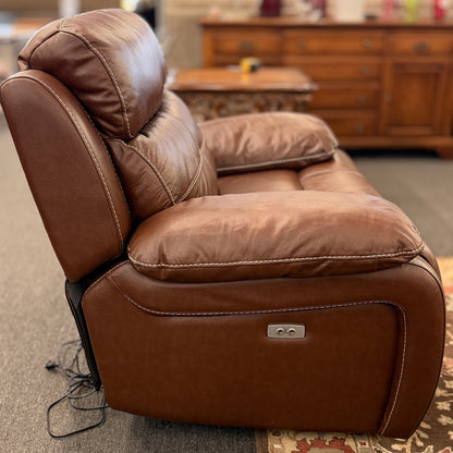 A large plush contemporary recliner upholstered in saddle brown leather with pillow-top armrests, segmented back cushioning, and light topstitching in excellent condition.