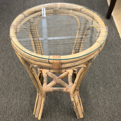 A small round end table with a bent organic-style bamboo frame, wrapped structural joints, an X-shaped cross-stretcher, and a clear glass tabletop.
