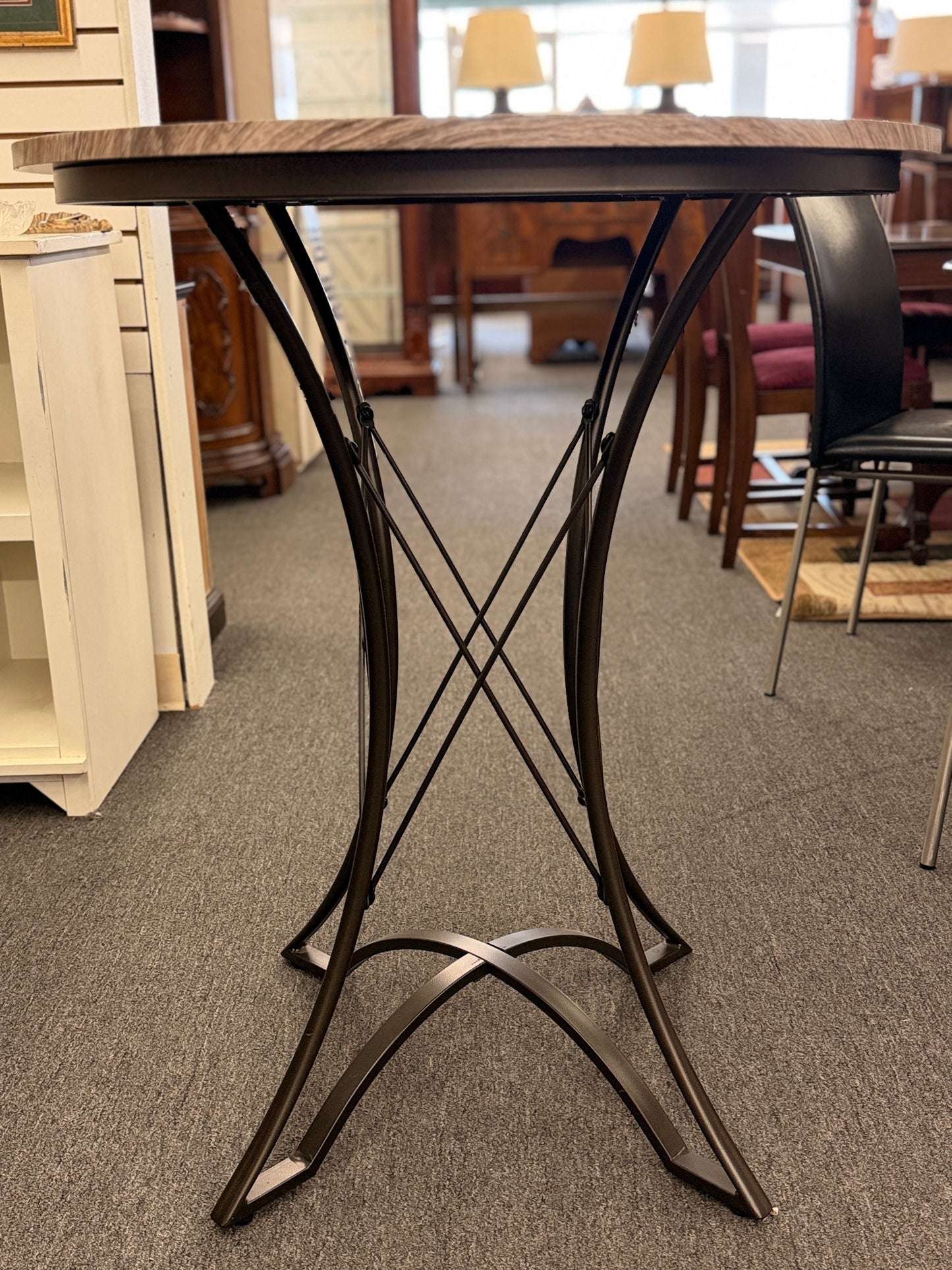 Round pub table with a light brownish-grey faux wood grain top and a dark metal pedestal base featuring curved intersecting legs.