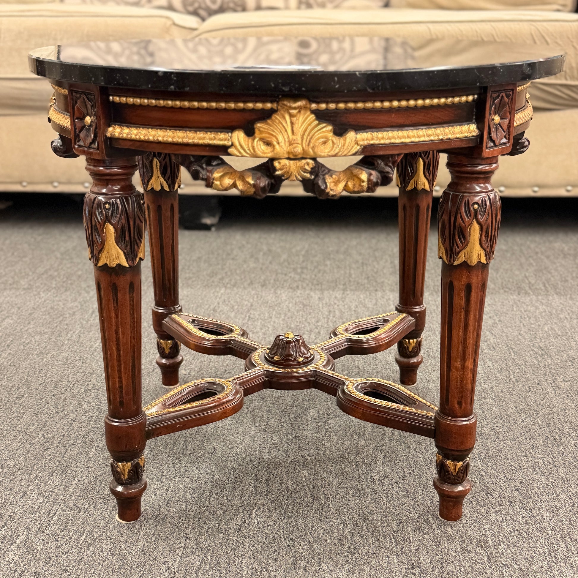 Round accent table featuring a dark marble top, ornate carved wooden base with gold-painted detailing, and a decorative cross-stretcher.