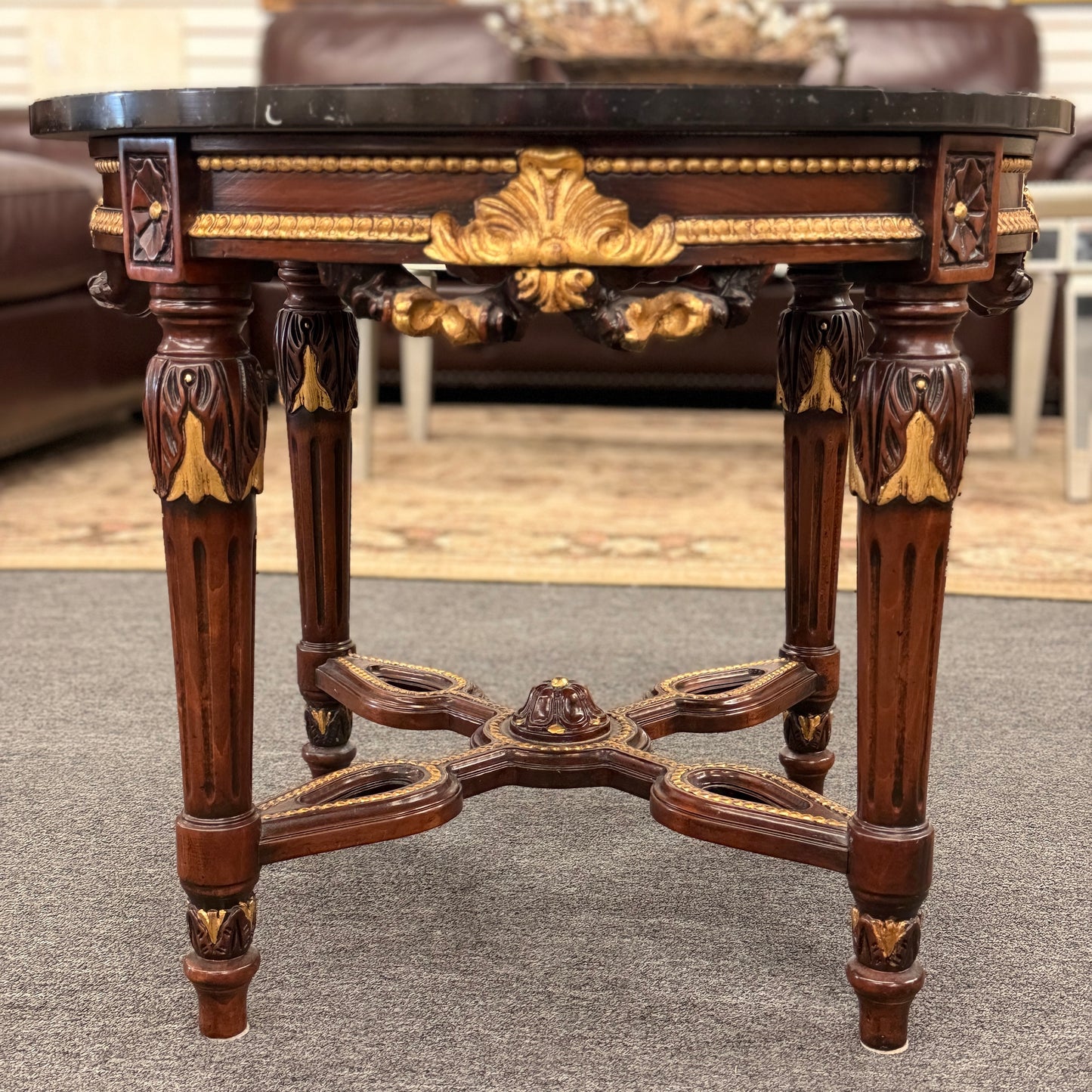 Round accent table featuring a dark marble top, ornate carved wooden base with gold-painted detailing, and a decorative cross-stretcher.