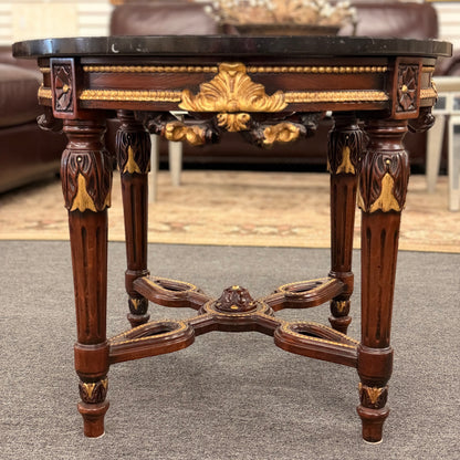 Round accent table featuring a dark marble top, ornate carved wooden base with gold-painted detailing, and a decorative cross-stretcher.