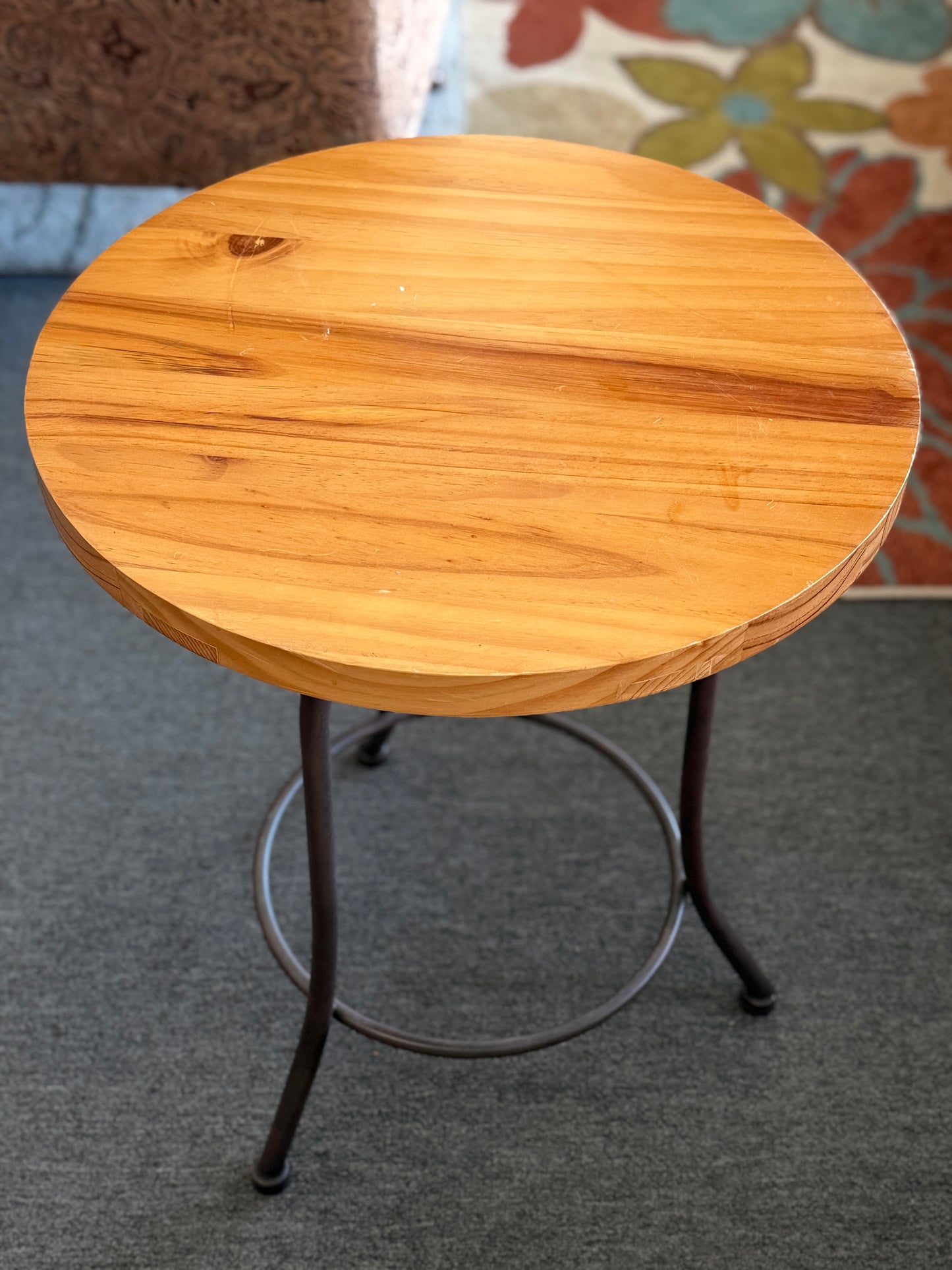 Round accent table featuring a natural wood plank-style top and a slender curved dark metal pedestal base with a lower support ring.