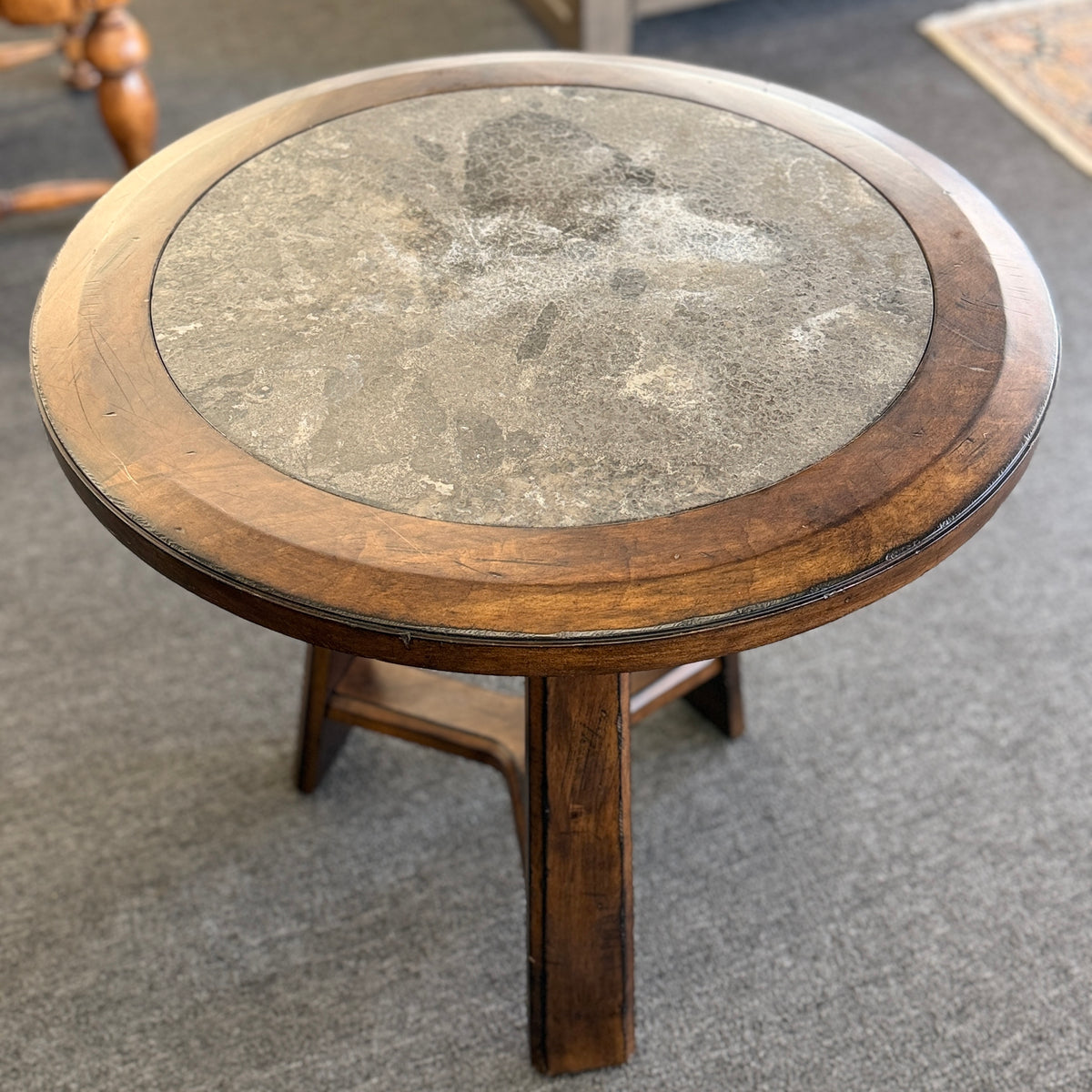 A round wooden side accent table featuring a rustic mottled stone or slate inlay top set over a sturdy pedestal-style base in good condition.