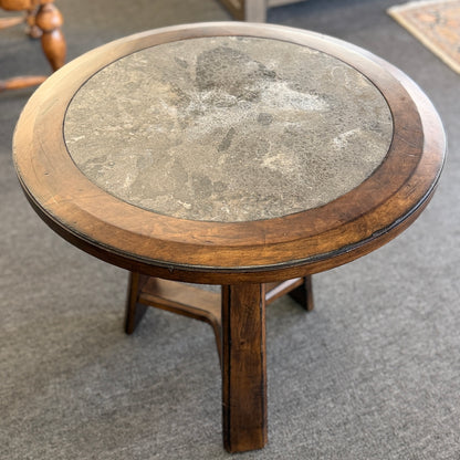 A round wooden side accent table featuring a rustic mottled stone or slate inlay top set over a sturdy pedestal-style base in good condition.
