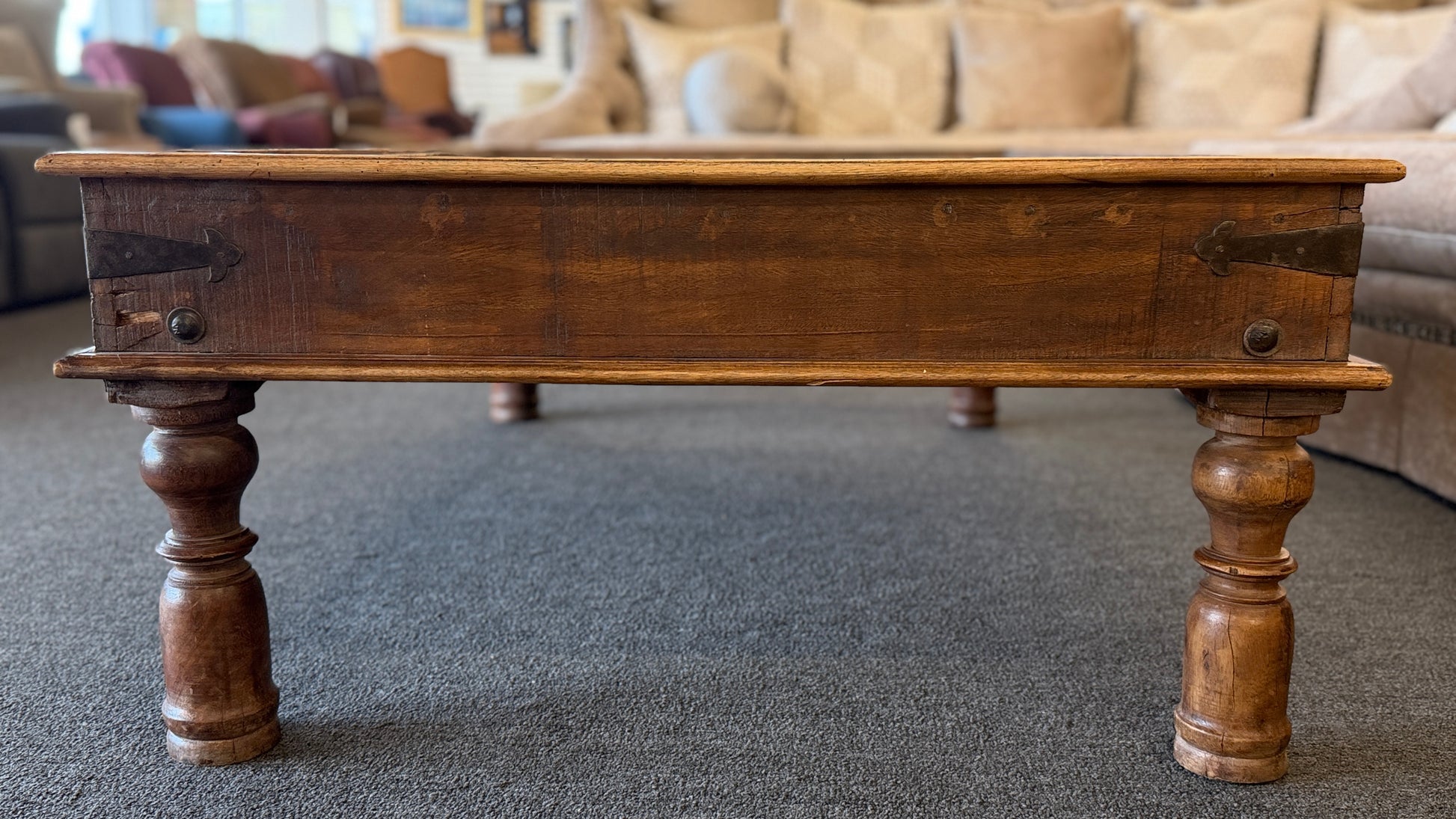 A rustic low-profile wooden coffee table featuring a paneled top resembling a repurposed antique door with decorative metal hinges and turned wooden legs.