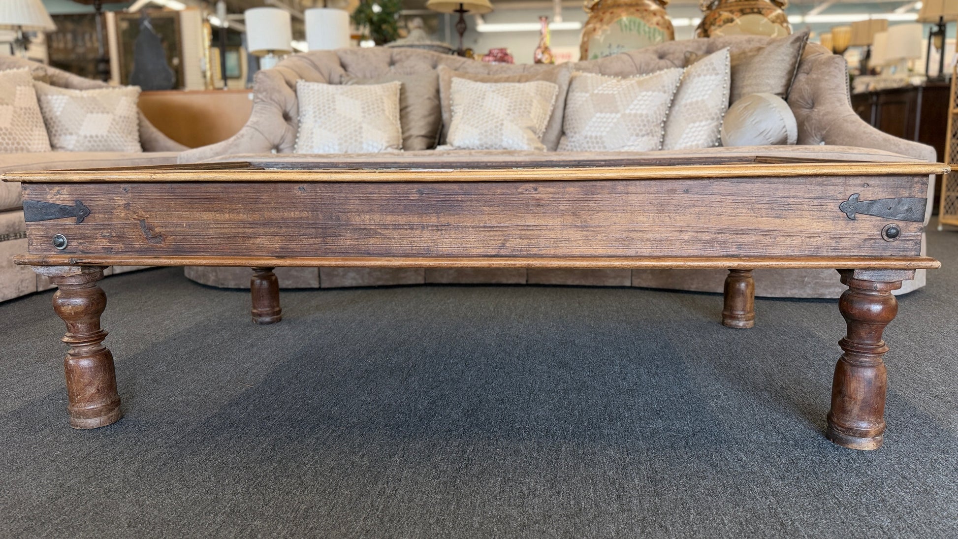 A rustic low-profile wooden coffee table featuring a paneled top resembling a repurposed antique door with decorative metal hinges and turned wooden legs.