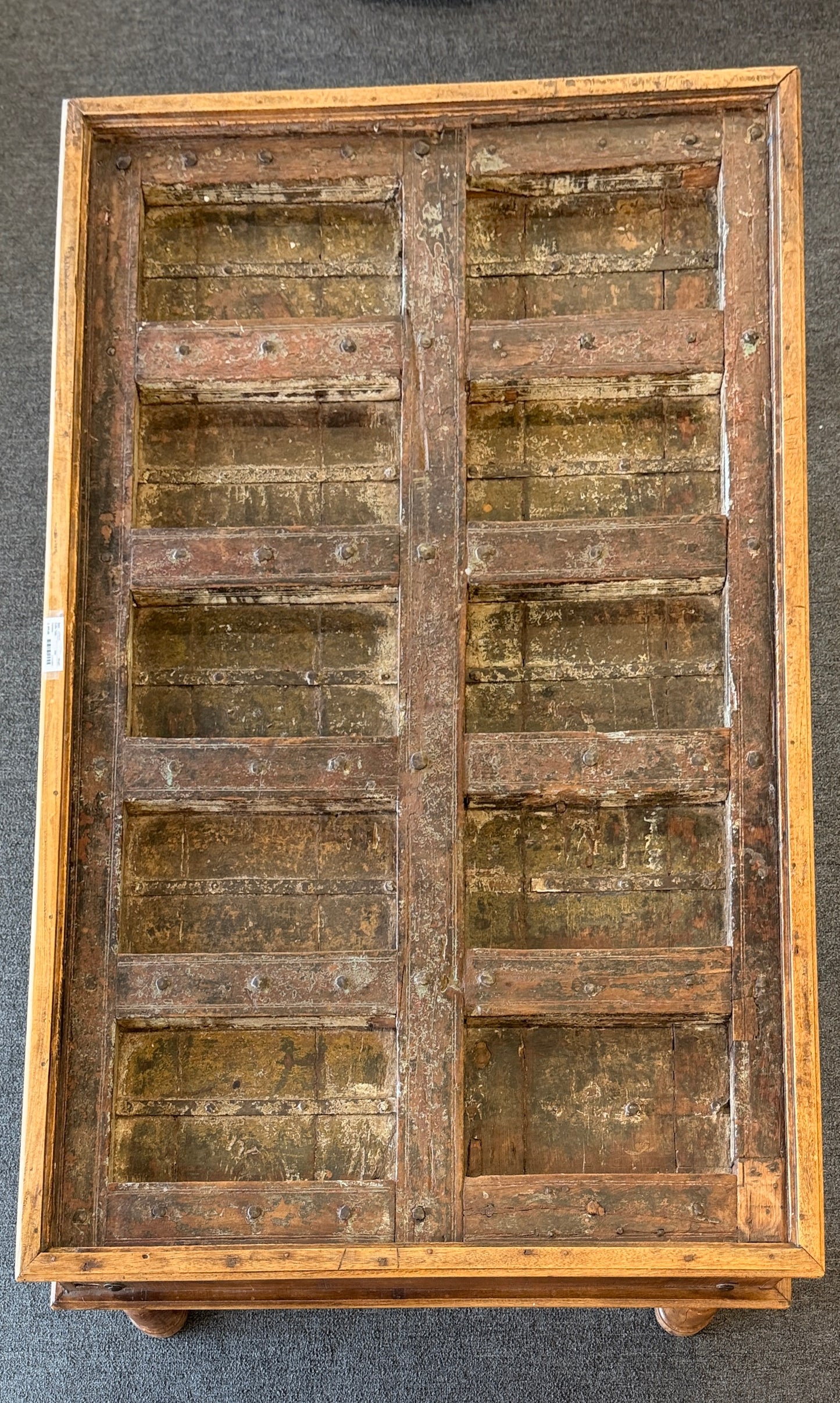 A rustic low-profile wooden coffee table featuring a paneled top resembling a repurposed antique door with decorative metal hinges and turned wooden legs.