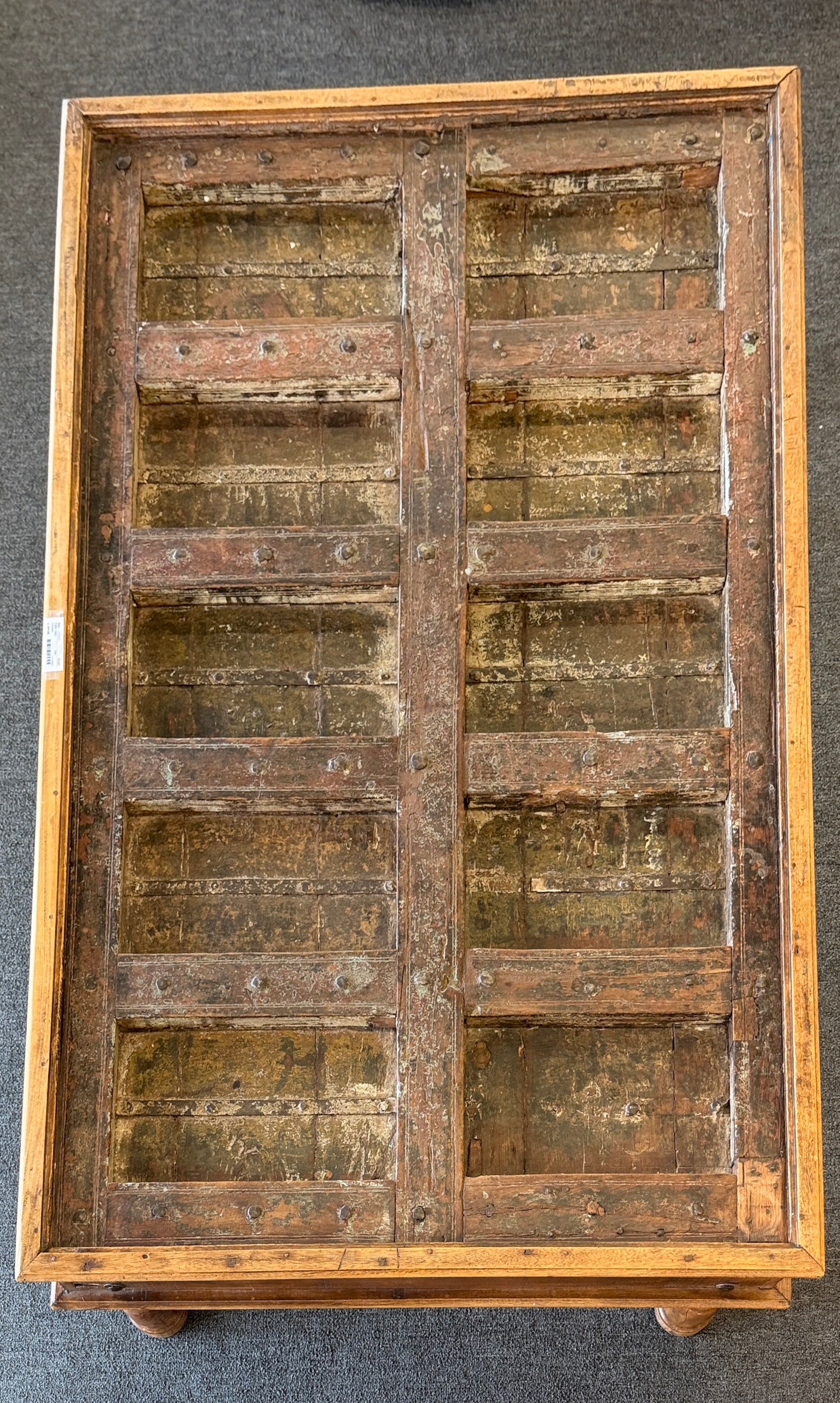 A rustic low-profile wooden coffee table featuring a paneled top resembling a repurposed antique door with decorative metal hinges and turned wooden legs.