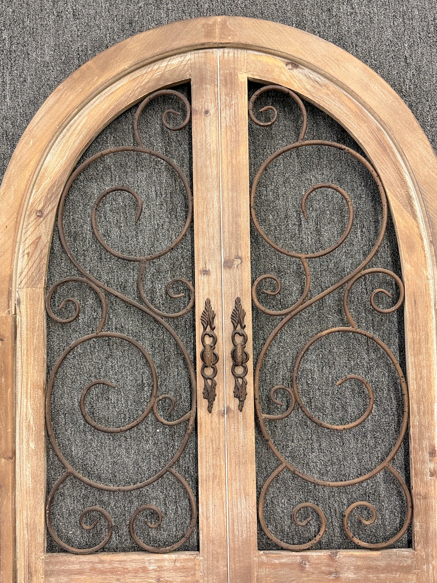 A large arched decorative wall panel designed like a rustic Tuscan door with a distressed wood frame and dark metal scrollwork gating.