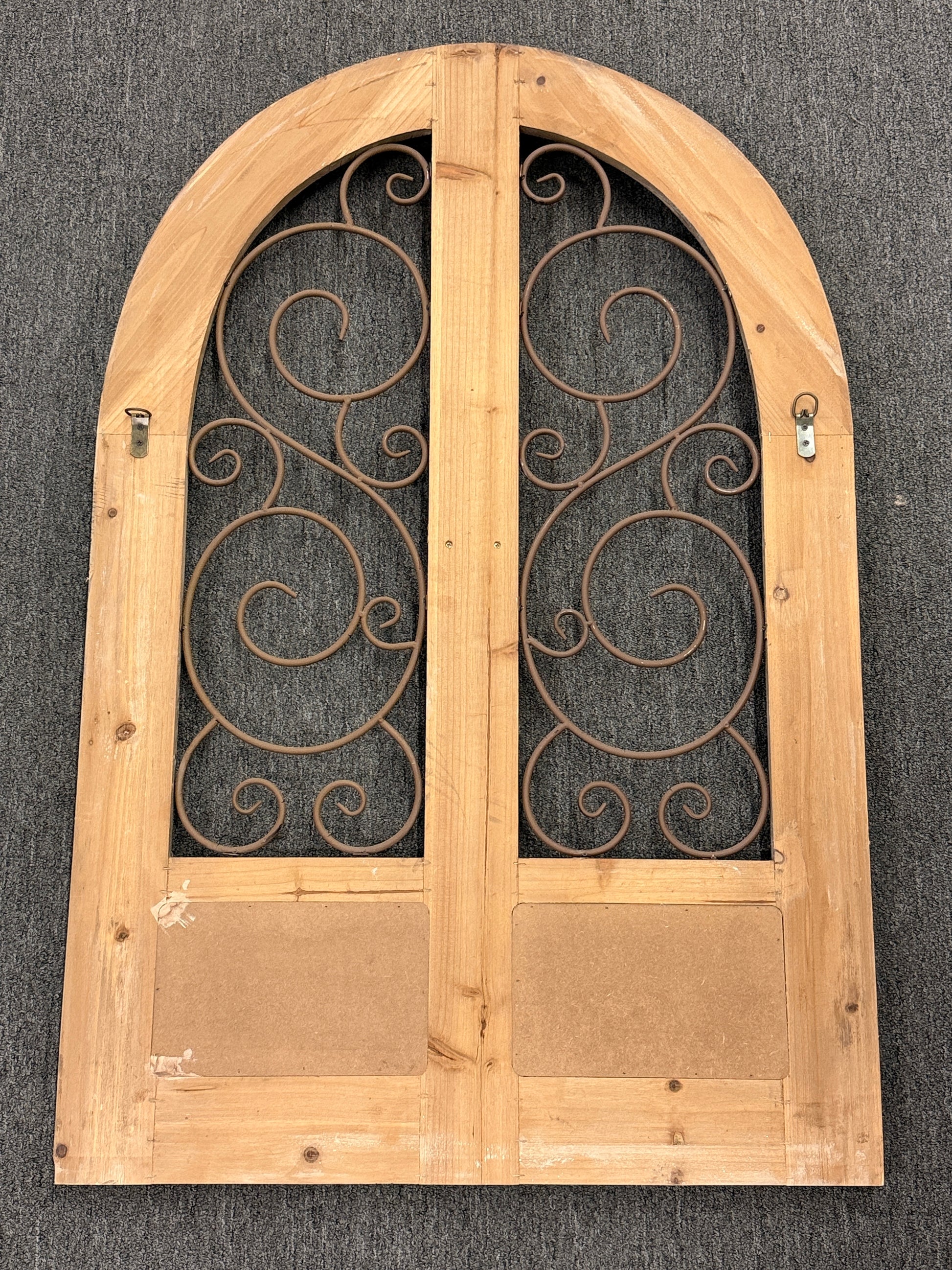A large arched decorative wall panel designed like a rustic Tuscan door with a distressed wood frame and dark metal scrollwork gating.
