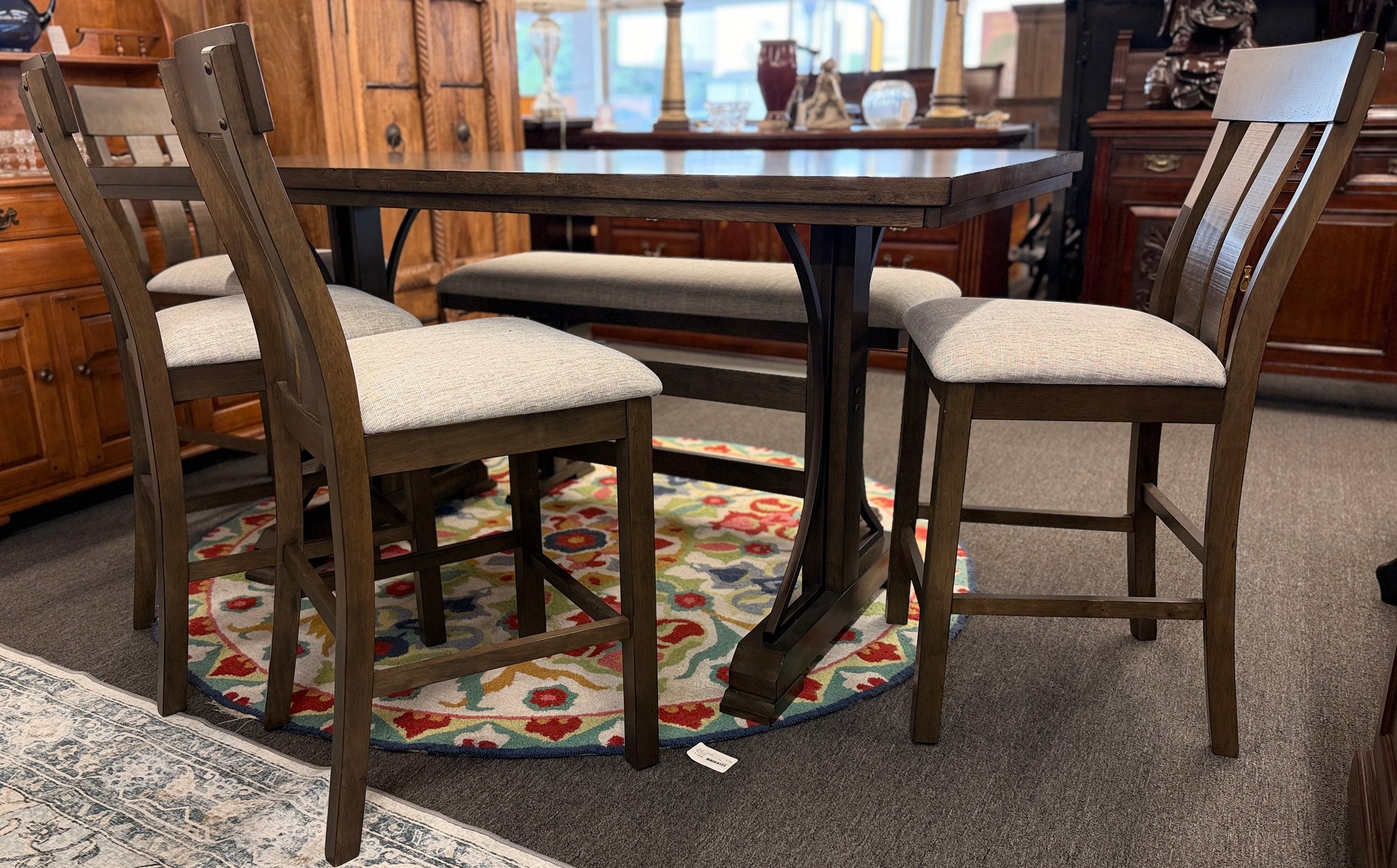 A rustic-modern counter-height dining set featuring a long wood and iron table, four matching slat-back chairs, and a long upholstered dining bench.