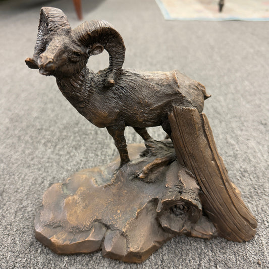 A rustic figurine depicting a ram standing on a rocky outcrop next to a broken tree stump.