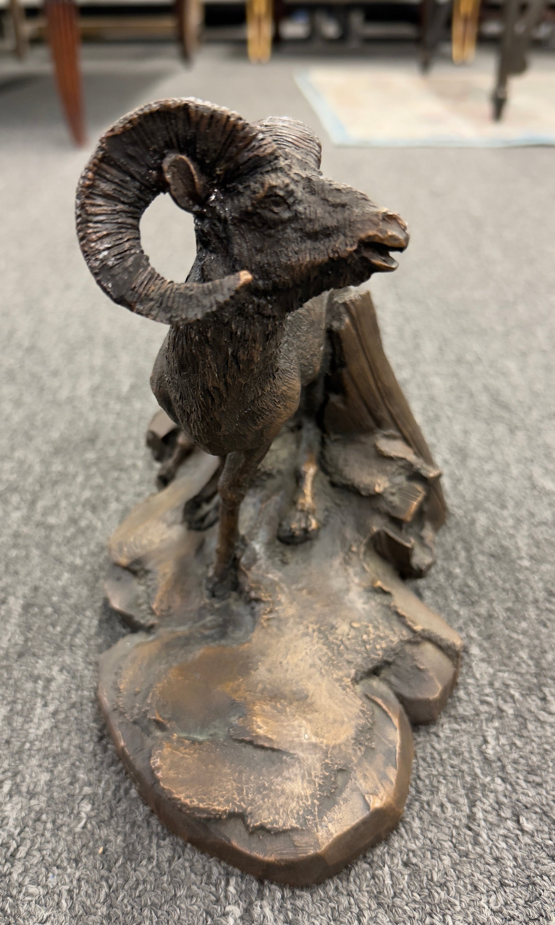 A rustic figurine depicting a ram standing on a rocky outcrop next to a broken tree stump.