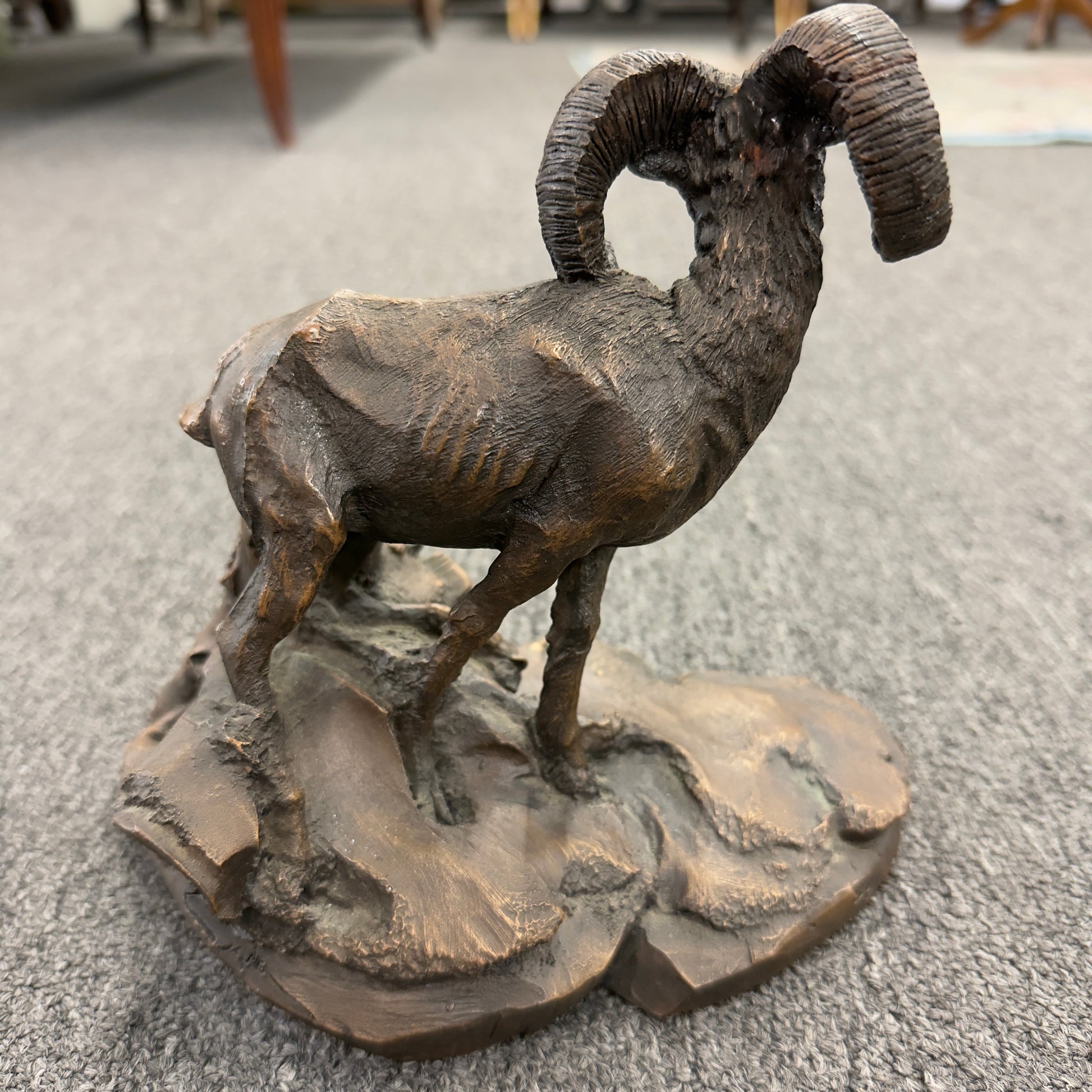 A rustic figurine depicting a ram standing on a rocky outcrop next to a broken tree stump.