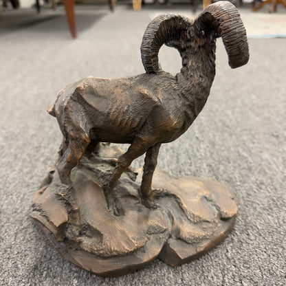 A rustic figurine depicting a ram standing on a rocky outcrop next to a broken tree stump.