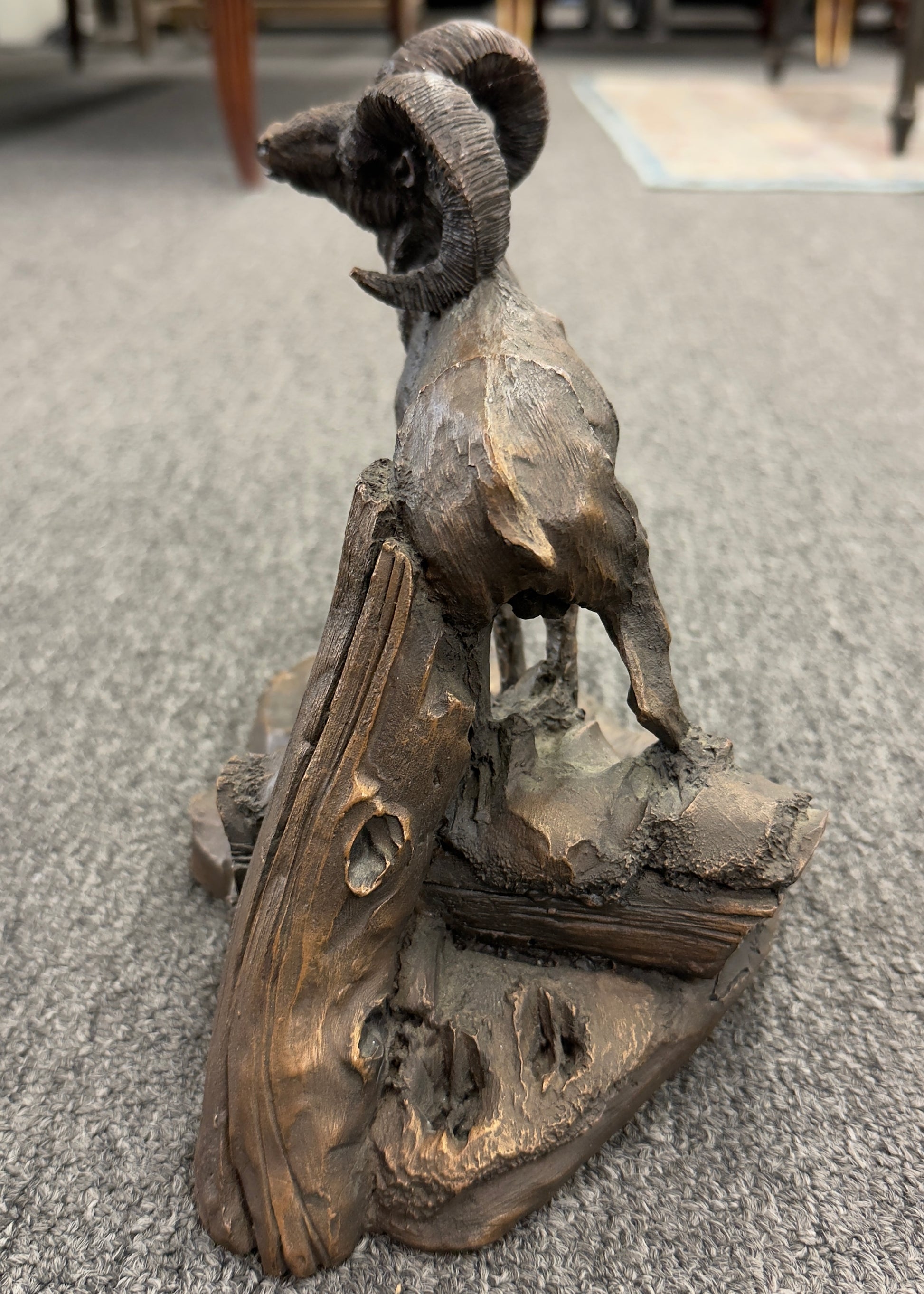 A rustic figurine depicting a ram standing on a rocky outcrop next to a broken tree stump.