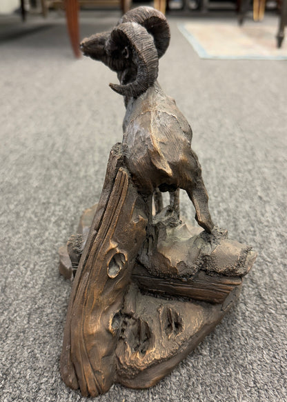 A rustic figurine depicting a ram standing on a rocky outcrop next to a broken tree stump.