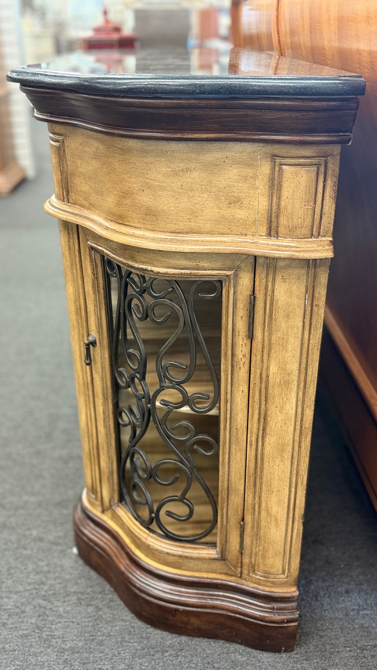 A rustic traditional wooden server featuring a curved silhouette, two top drawers, a dark top, and two glass doors with ornate metal scrollwork.