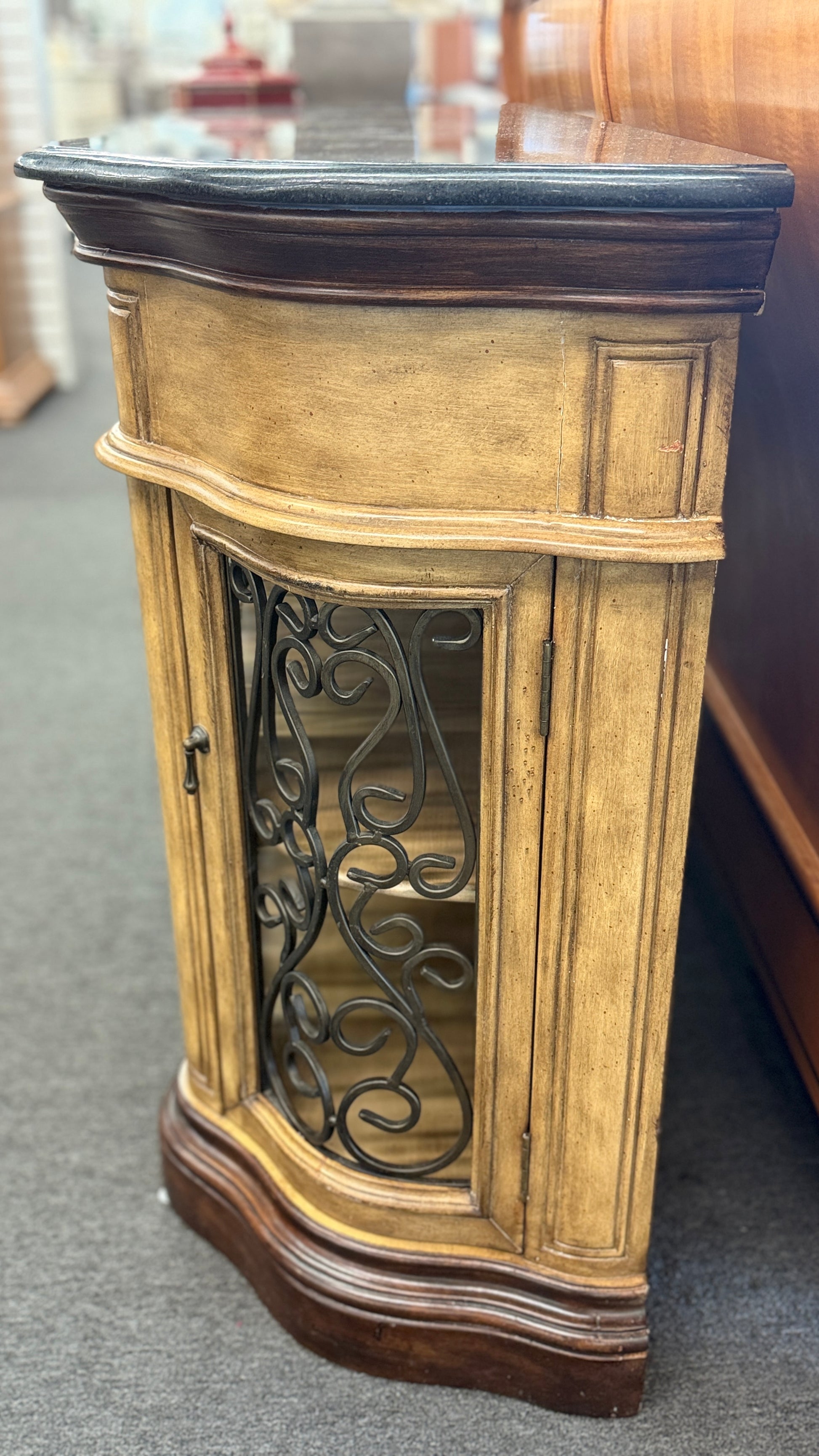 A rustic traditional wooden server featuring a curved silhouette, two top drawers, a dark top, and two glass doors with ornate metal scrollwork.