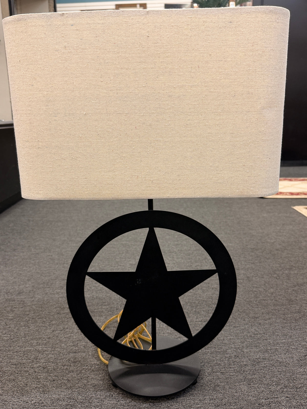 A rustic western-style table lamp featuring a black metal star-in-circle silhouette base topped with a rectangular off-white linen drum shade in good condition.