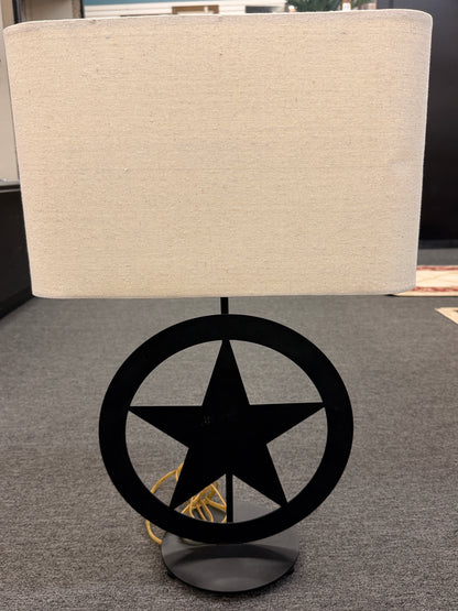 A rustic western-style table lamp featuring a black metal star-in-circle silhouette base topped with a rectangular off-white linen drum shade in good condition.