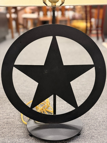 A rustic western-style table lamp featuring a black metal star-in-circle silhouette base topped with a rectangular off-white linen drum shade in good condition.