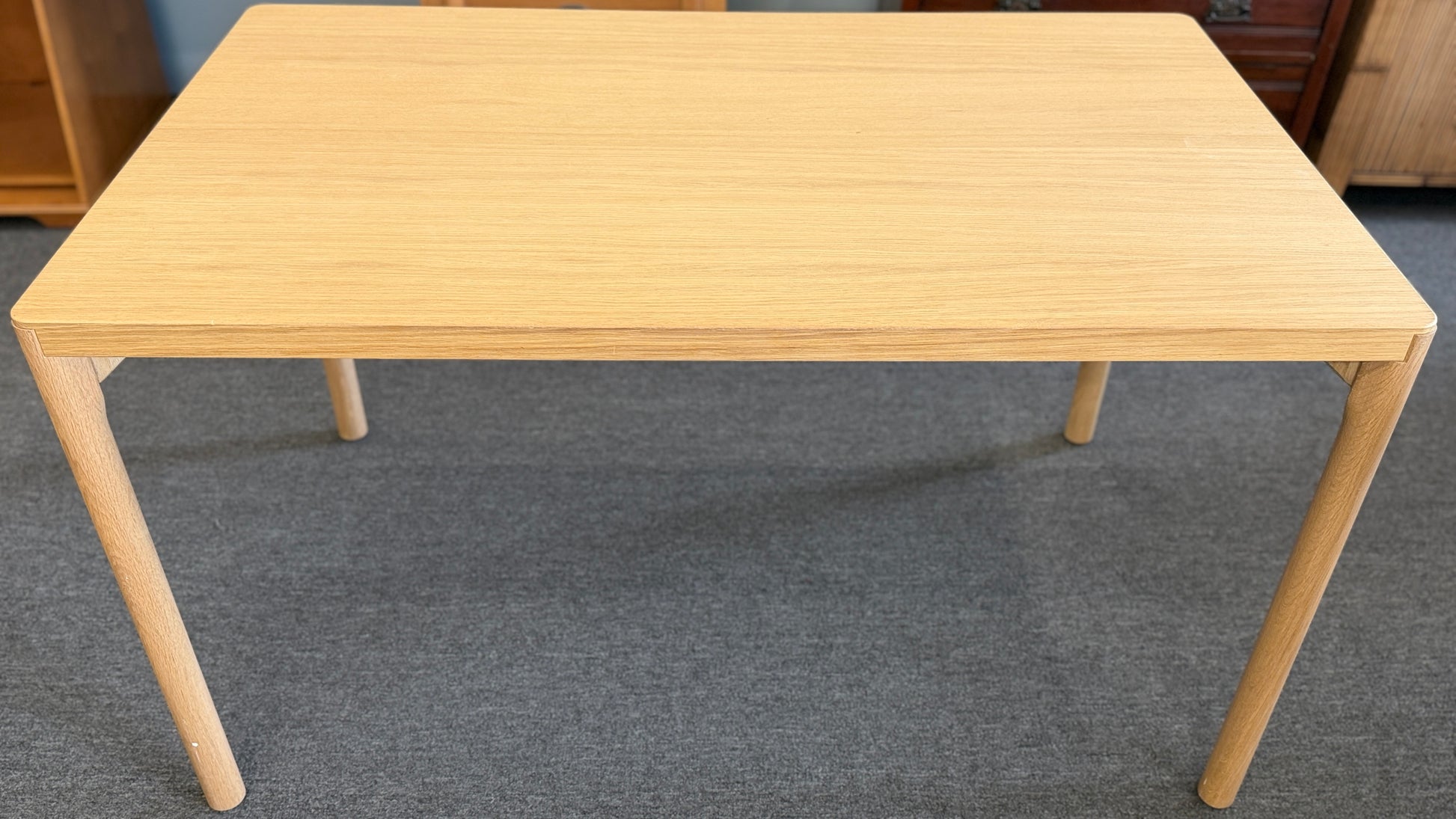 Scandinavian-style light wood writing desk featuring a rectangular tabletop with rounded corners and slightly splayed cylindrical wooden legs.