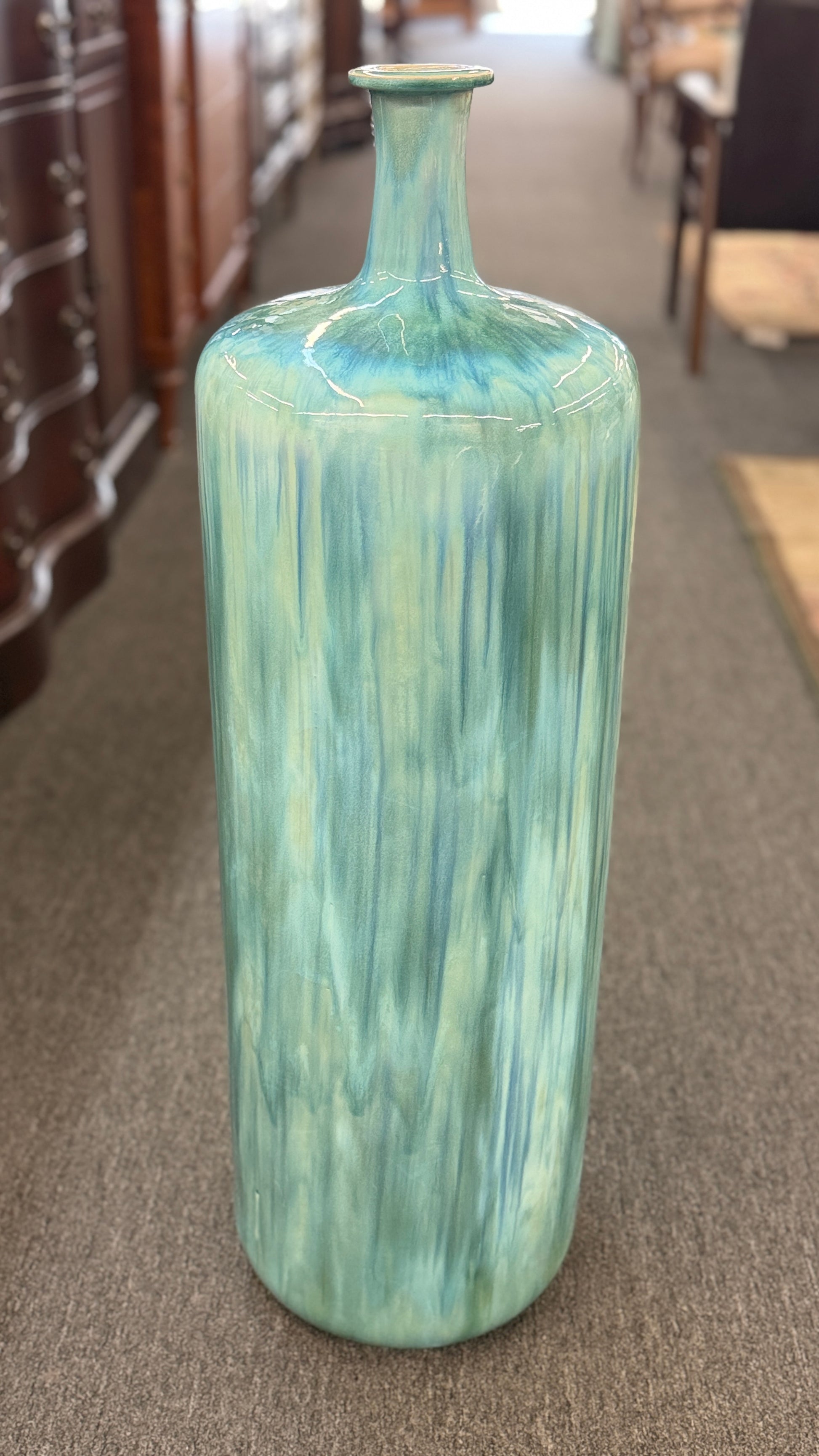 A tall, large cylindrical ceramic floor vase with a narrow neck, featuring a glossy, vertically streaked drip-glaze finish in seafoam green, aqua, and pale blue.
