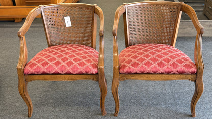 Set of two wooden armchairs featuring woven cane backrests, curved wooden arms, and red upholstered seats with a light geometric pattern.